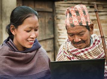A young woman and an older man in Nepal smiling at a laptop