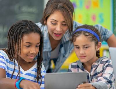 A teacher and two elementary students reading together on a tablet in a classroom