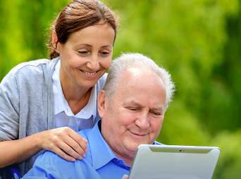 A woman and an older man reading together on a tablet outdoors