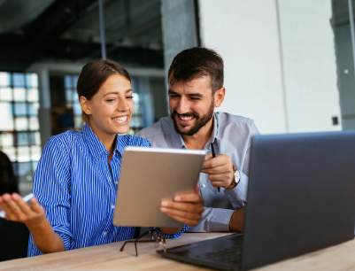 Two colleagues smiling while reviewing content on a tablet at work
