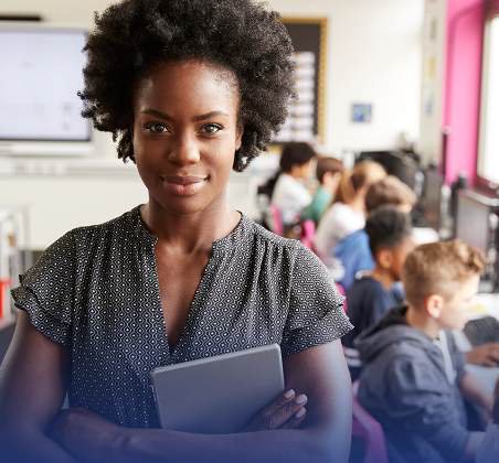 A teacher holding a tablet in a colorful classroom